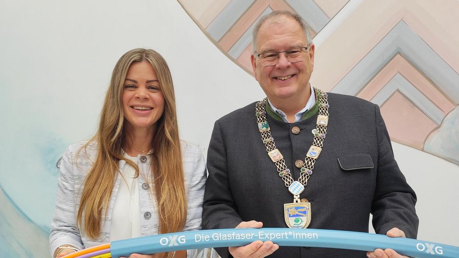 Zwei Personen, ein Mann und eine Frau, stehen nebeneinander und halten zusammen ein Exponat eines Glasfaserkabels.