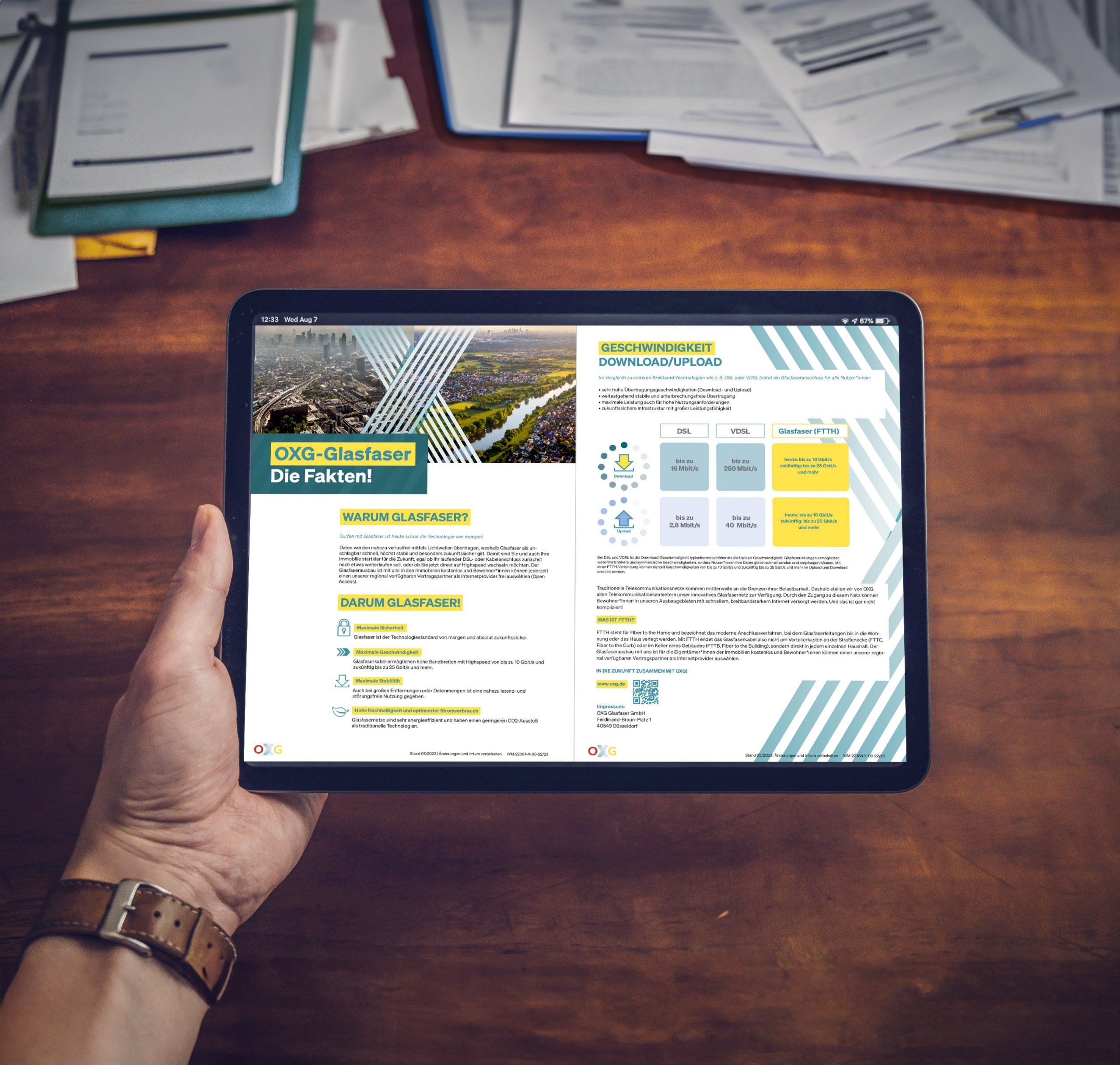 Tablet, das eine Informationsgrafik zu OXG-Glasfaser mit Daten zu Geschwindigkeit, Download und Upload zeigt, liegt auf einem Holztisch