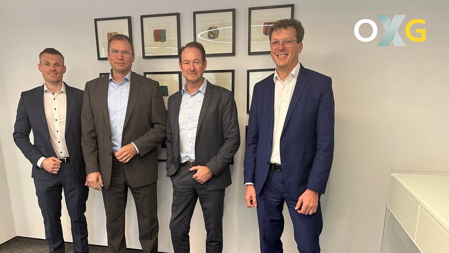 Vier männliche Personen in formeller Kleidung stehen in einem modernen Büro vor einer Wand mit gerahmten Kunstwerken anlässlich der Partnerschaft von OXG, Vodafone und dem Spar- und Bauverein eG Dortmund zur digitalen Grundversorgung durch Glasfaser