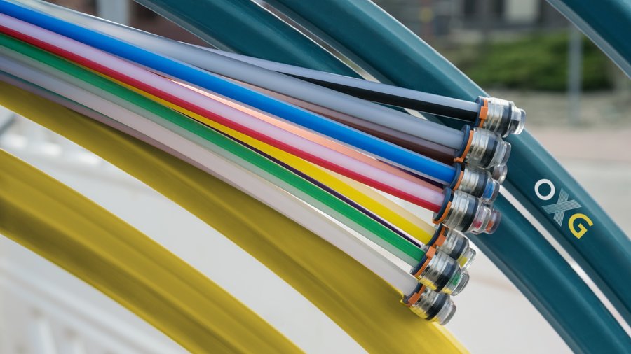 Bunte Schläuche mit Anschlüssen liegen übereinander auf einer Oberfläche, während im Hintergrund einige grüne Schlauchvarianten sichtbar sind