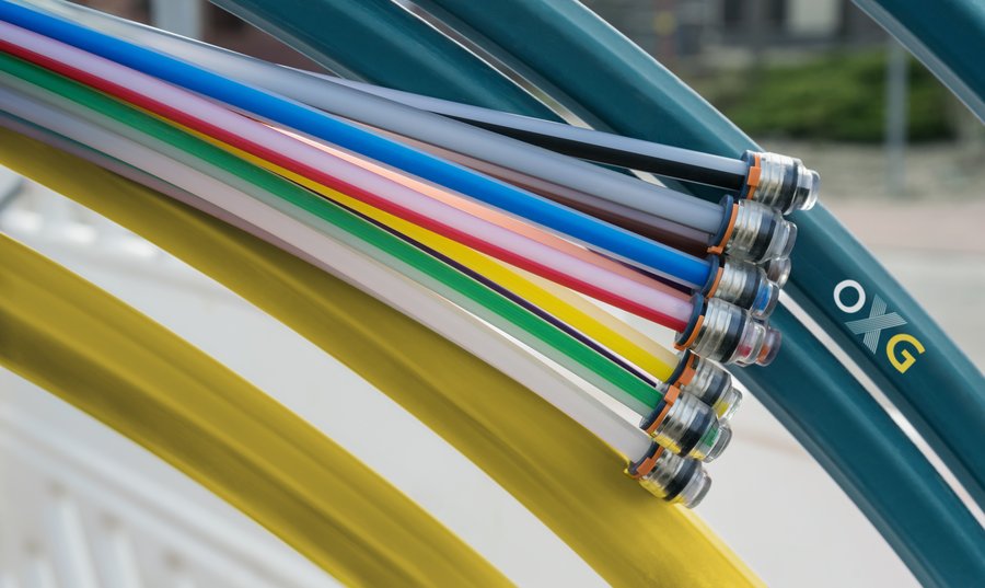 Bunte Schläuche mit Anschlüssen liegen übereinander auf einer Oberfläche, während im Hintergrund einige grüne Schlauchvarianten sichtbar sind
