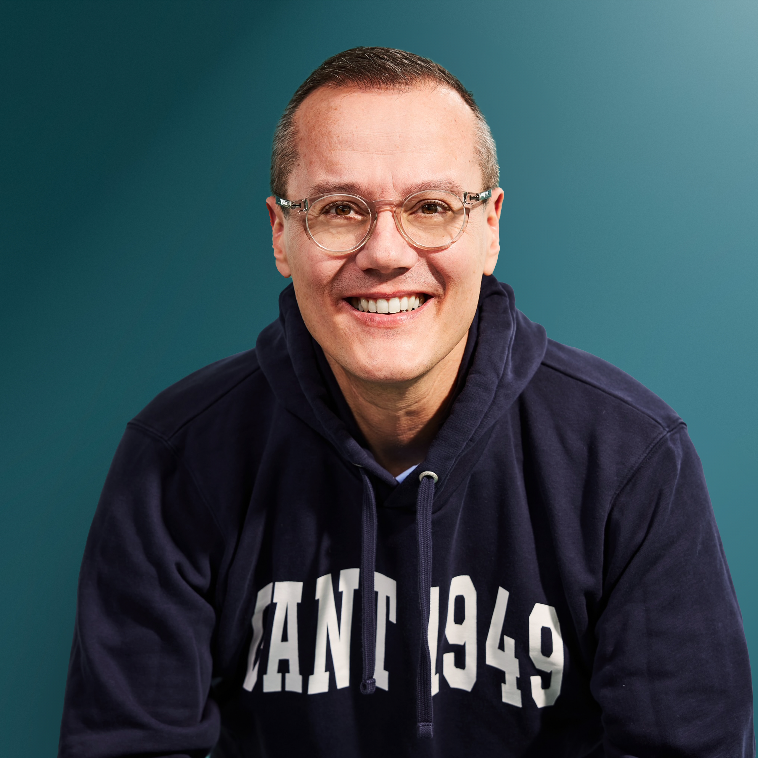 Lächelnder Mann mit Brille in einem dunkelblauen Hoodie vor einem einfarbigen Hintergrund
