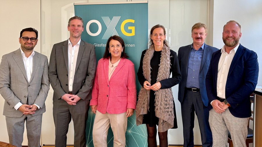 Sechs Personen in formeller Kleidung posieren vor einem Banner „OXG – Glasfaser für alle“ anlässlich der Vertragsunterzeichnung zum Glasfaserausbau in der Region Hof.
