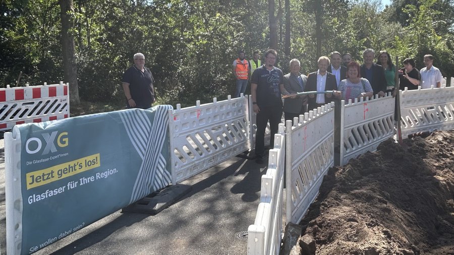 Gruppenfoto von Mitarbeitern und Partnern der OXG an einer Baustelle in Duisburg für den Glasfaserausbau, umgeben von Bauzäunen und Erdarbeiten