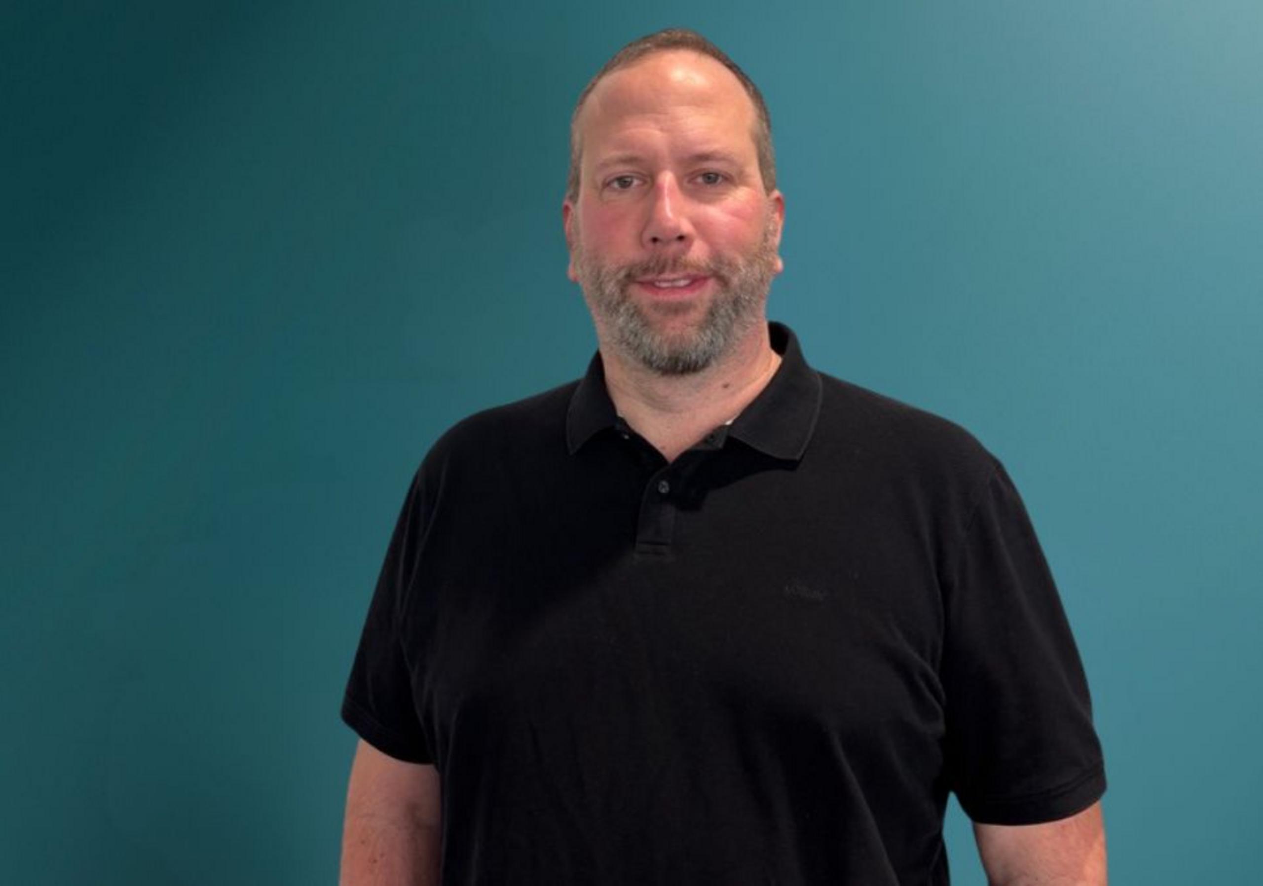 Porträt eines Mannes mit schwarzem T-Shirt, der vor einem türkisfarbenen Hintergrund steht