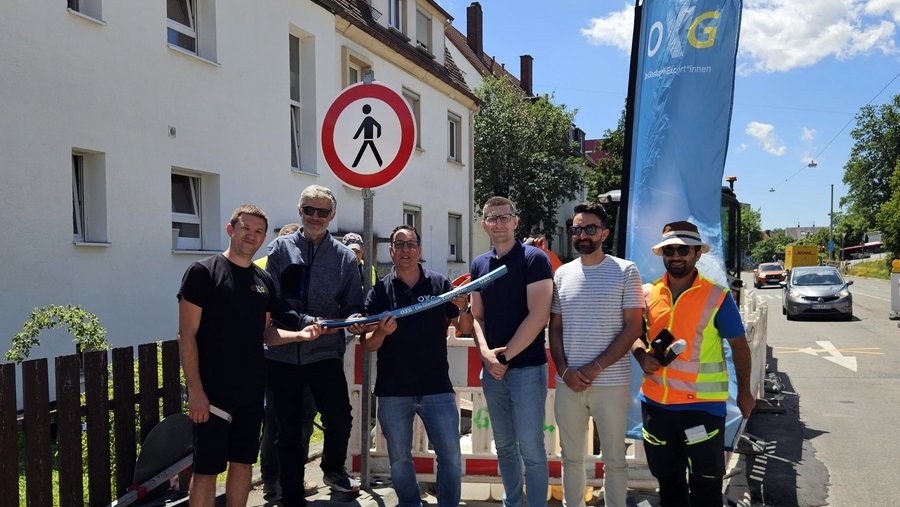 Gruppenfoto von Mitarbeitern der OTG, die auf einer Baustelle in Ulm stehen und eine blaue Rohre halten, mit einem Verkehrszeichen und einem Banner im Hintergrund
