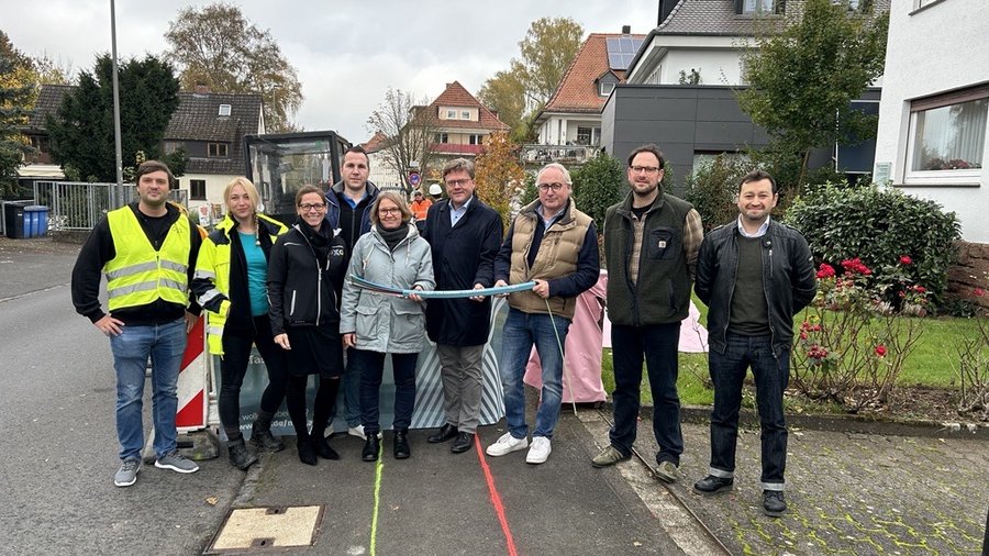 Gruppenbild von mehreren Personen, die gemeinsam ein Band bei einer Eröffnungsfeier in Marburg halten, während im Hintergrund Wohnhäuser und ein Bauzaun sichtbar sind