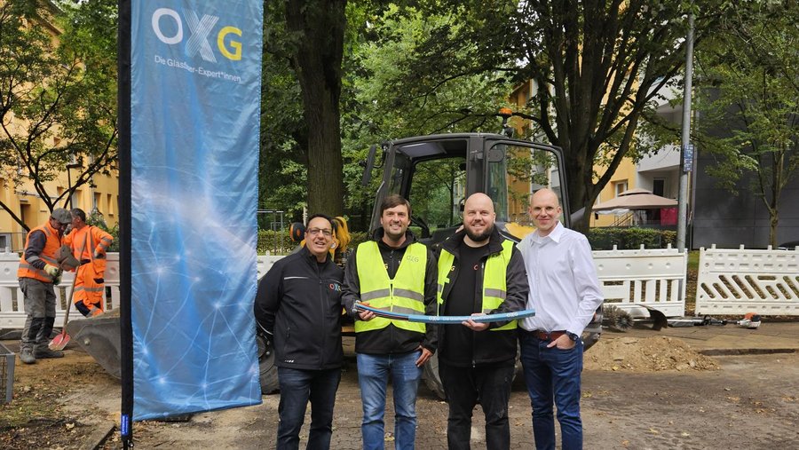 Gruppenfoto von Mitarbeitern der OXG, die an einer Baufläche n Karlsruhe stehen, während sie einen symbolischen Bauherrenakt mit einem blauen Band durchführen