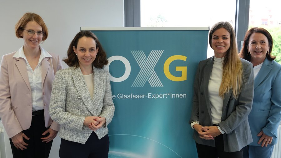 Vier Frauen stehen vor einem Plakat mit der Aufschrift „OXG – die Glasfaser-Expert*innen“ in einem modernen Büro in Nürnberg.