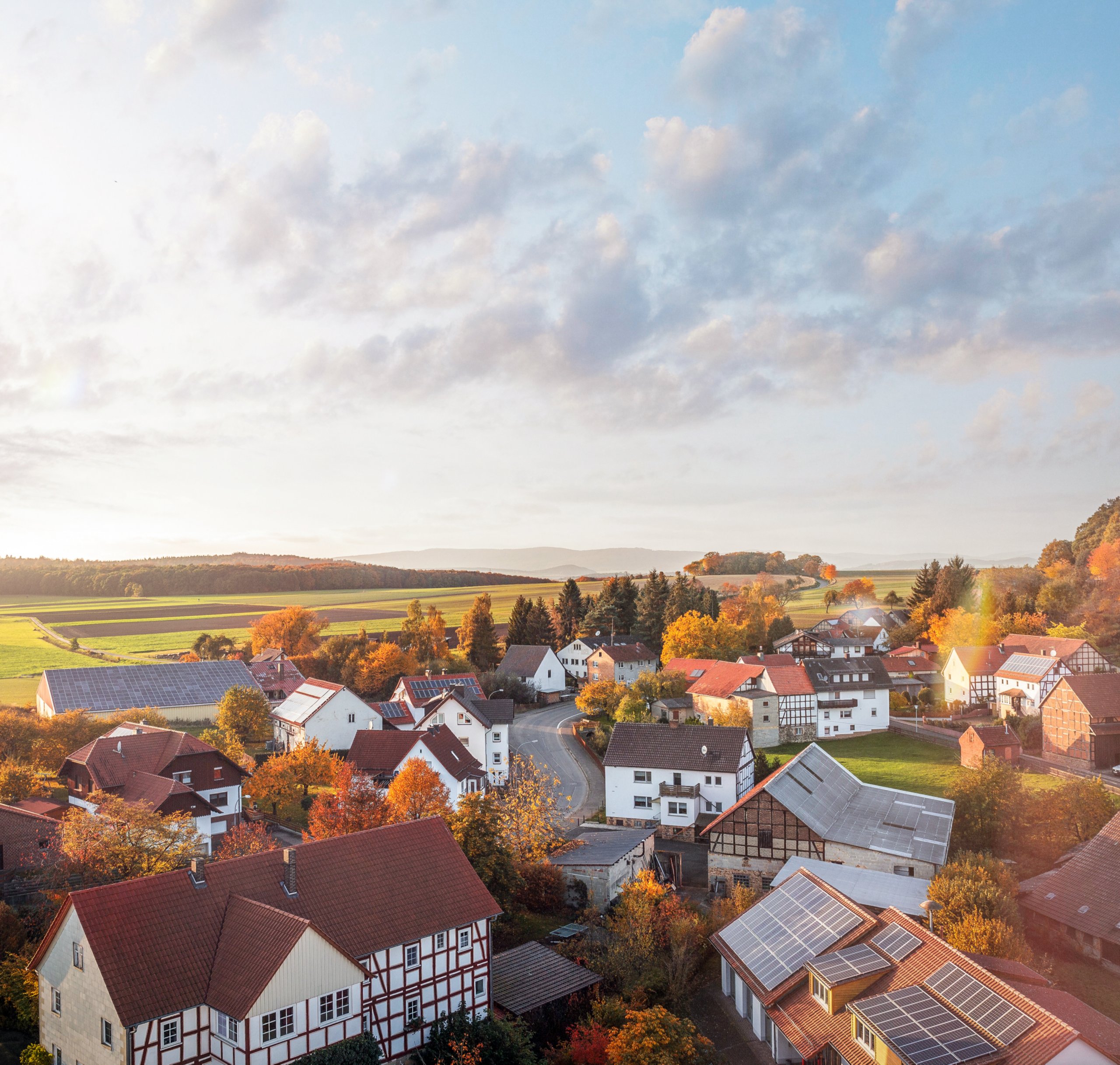 Landschaftsblick auf eine malerische Gemeinde mit Einfamilienhäusern, buntem Herbstlaub und sanften Hügeln im Hintergrund