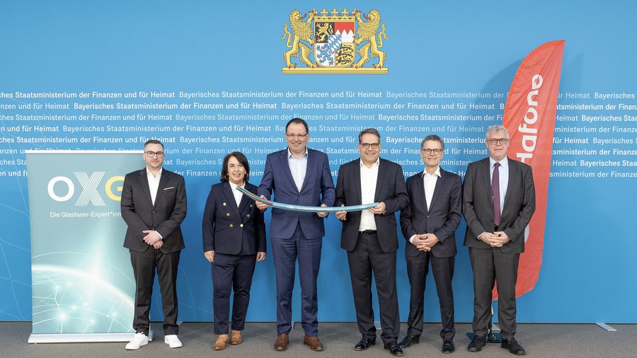 Die Presseveranstaltung zur Einführung von Glasfaser-Technologie mit mehreren Anwesenden in Form von Vertretern der Firma OXG und Hafone, vor der Hintergrundwand des Bayerischen Staatsministeriums für Finanzen und Heimat