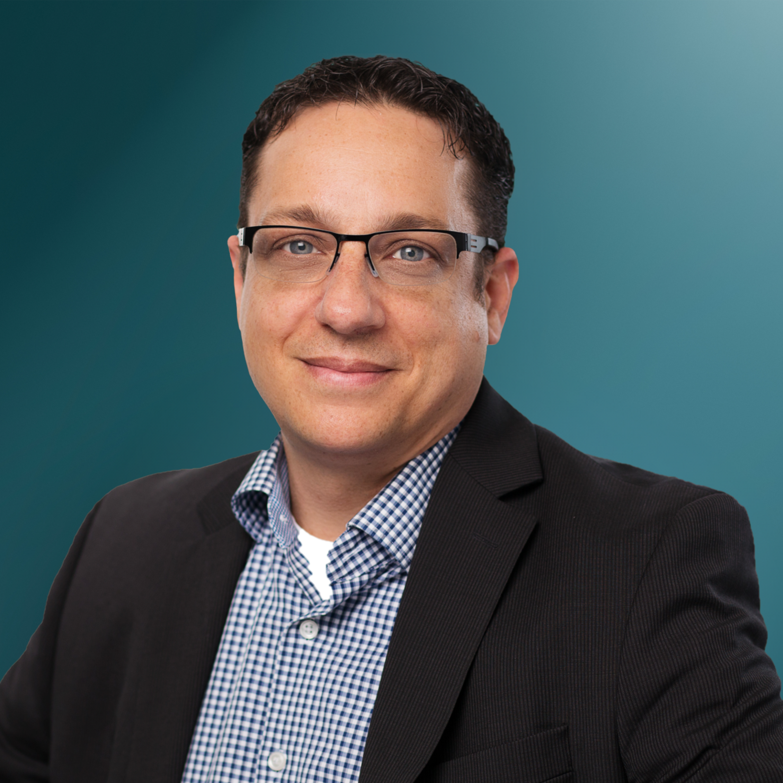 Professionelles Porträt eines Mannes mit Brille, der einen schwarzen Anzug und ein kariertes Hemd trägt, vor einem blauen Hintergrund