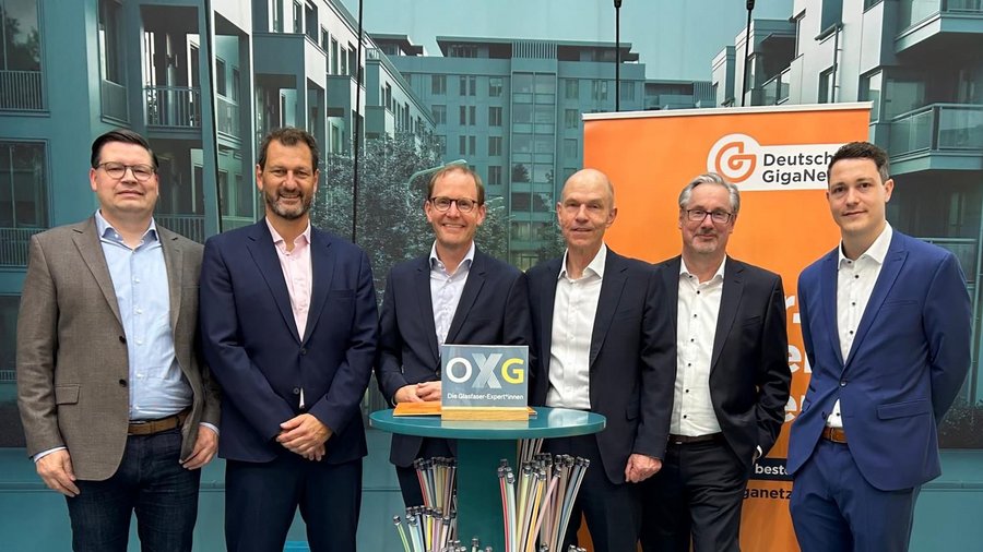 Eine Gruppe von sechs Männern auf einem Messestand. Sie stehen hinter einem Stehtisch zusammen, um ihre Partnerschaft zu feiern.