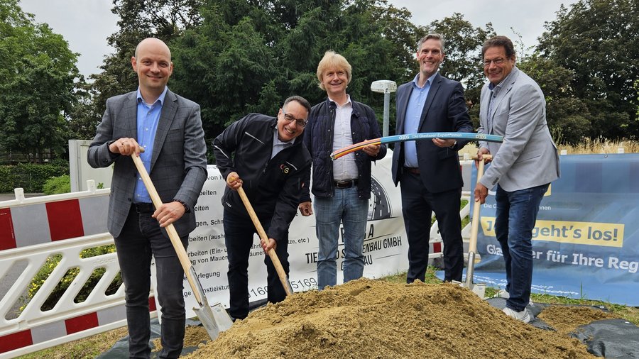 Gruppenfoto von fünf Personen bei einem symbolischen Spatenstich in Weingarten für ein Glasfaserprojekt, umgeben von Sand und Bauzäunen