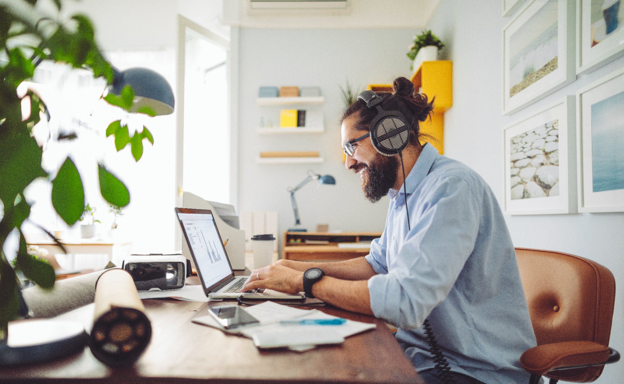 Mann mit Kopfhörern arbeitet am Laptop in einem modernen Homeoffice mit Pflanzen und hellen Farben