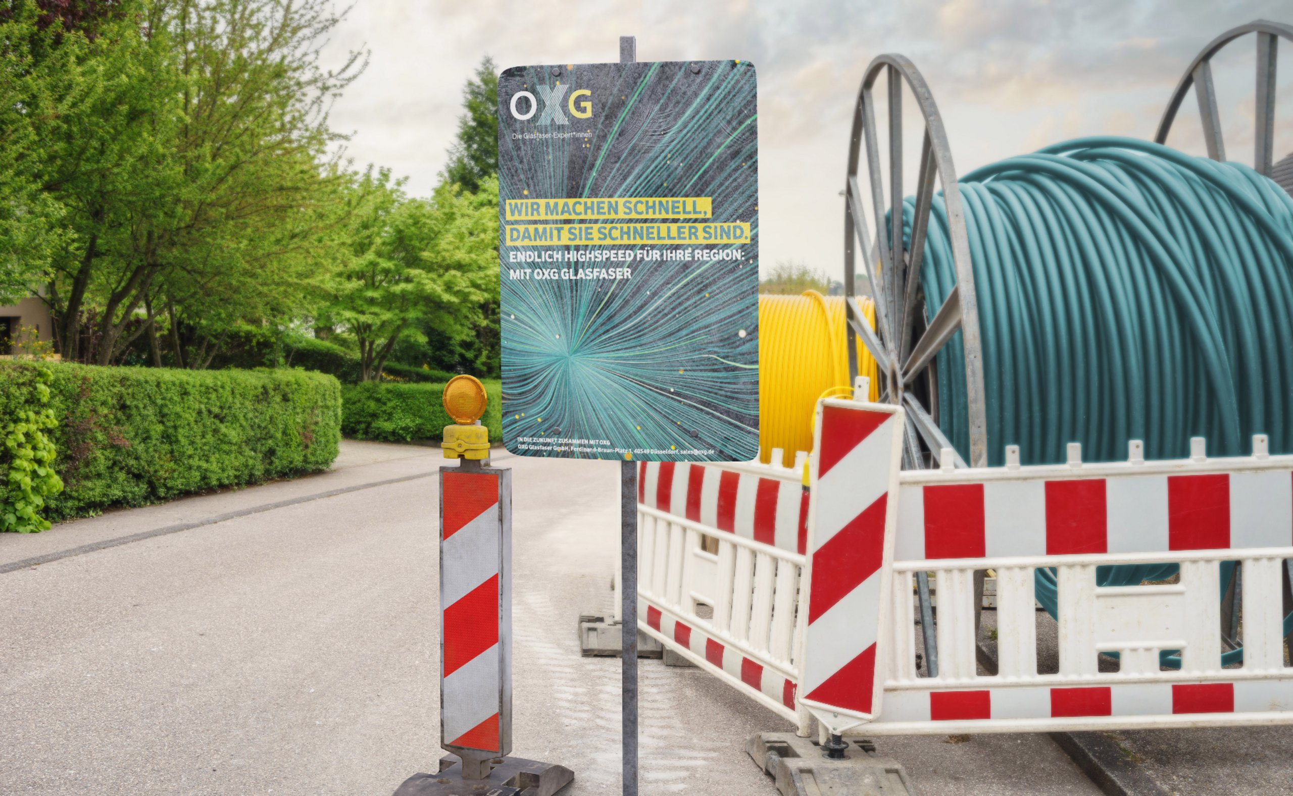 Plakat der OXG informiert über den Glasfaserausbau und weist auf eine Baustelle mit einer Absperrung hin