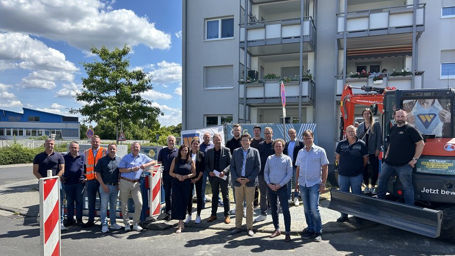 Gruppenfoto von Mitarbeitern und Beteiligten vor einem Bauprojekt in Wetzlar, umgeben von Baugeräten und einem Wohngebäude, unter einem klaren blauen Himmel mit Wolken